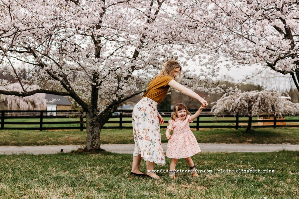 Mother and daughter dancing under blooming cherry blossom trees in Loudoun County.