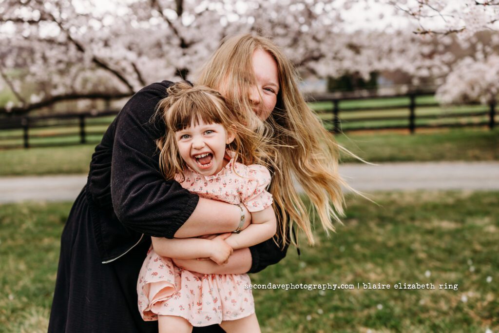 Au pair spinning girl under blooming cherry blossom trees in Loudoun County.