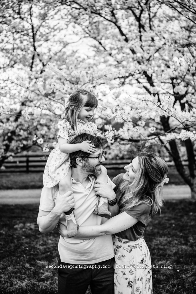 Family of 3 hugging under blooming cherry blossom trees in Loudoun County.
