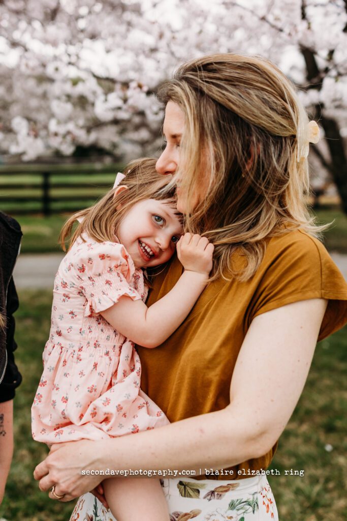 Mother and daughter hugging under blooming cherry blossom trees in Loudoun County.