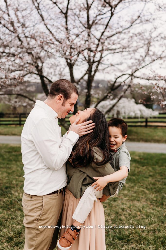 Family of 3 embracing under blooming cherry blossom trees in Loudoun County.