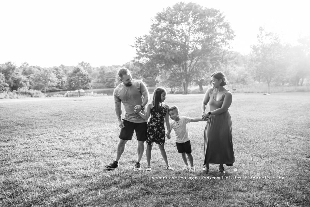Black and white image of family of 4 with sun behind them in a field.