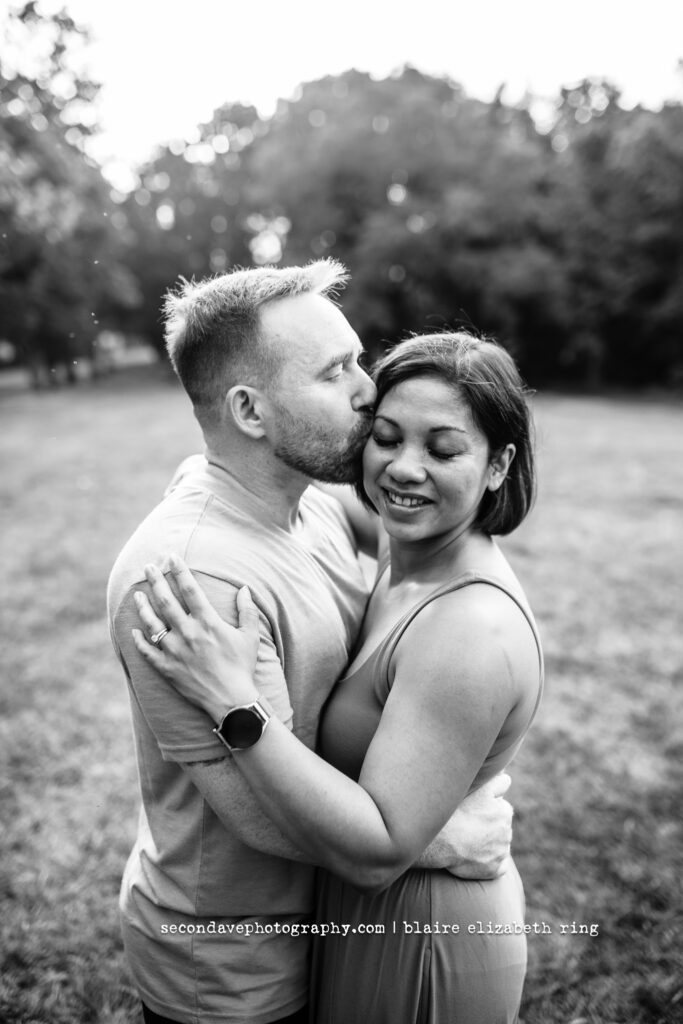 Black and white image of couple, with dad kissing mom on the temple.