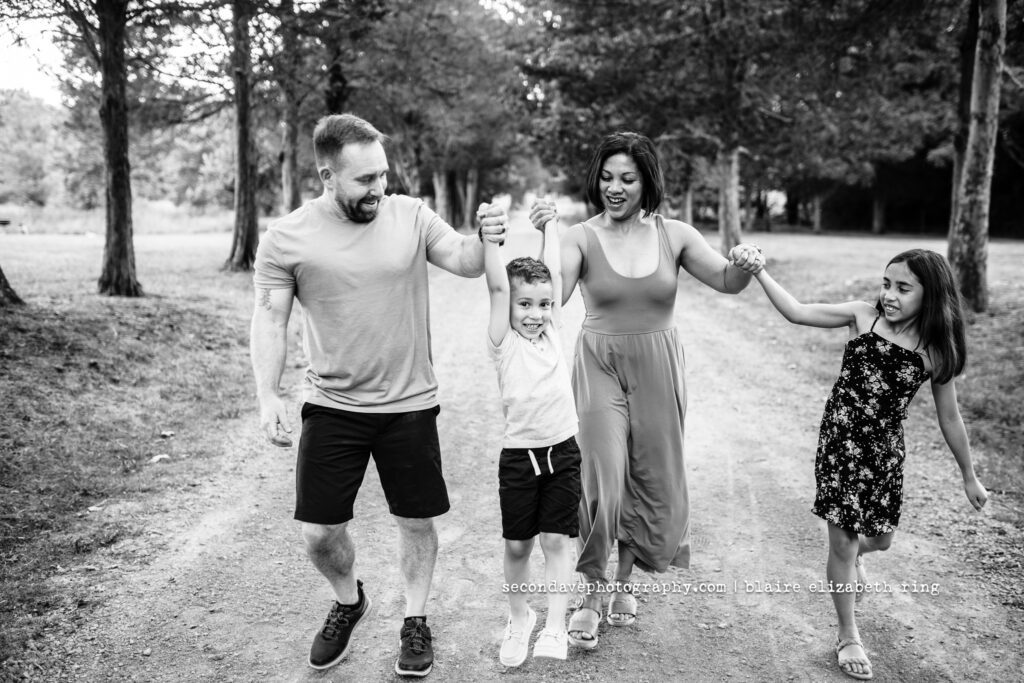Black and white photo of family of four swinging child.