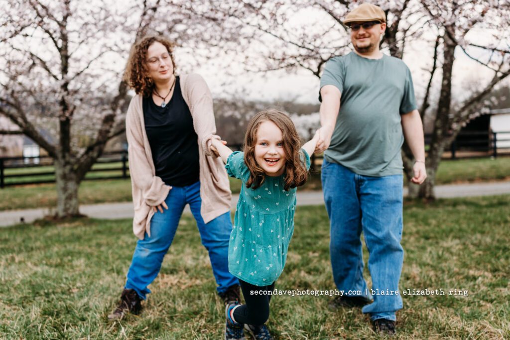 Family of 3 in front of blooming cherry blossoms in Northern Virginia.
