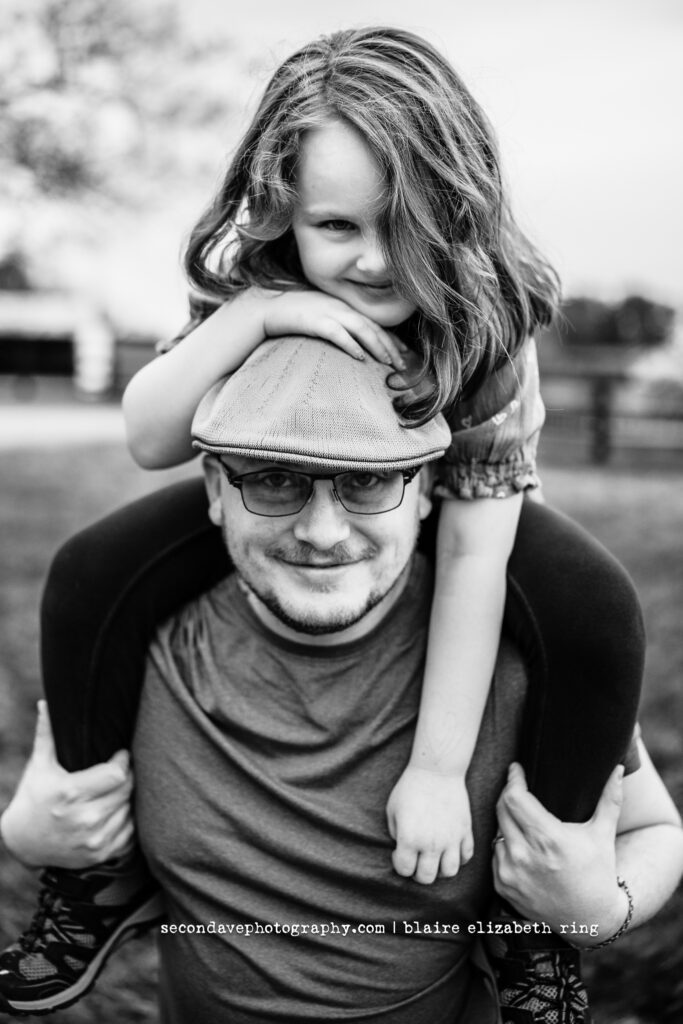 Black and white photo of daughter on dad's shoulders in front of blooming cherry blossoms in Northern Virginia.