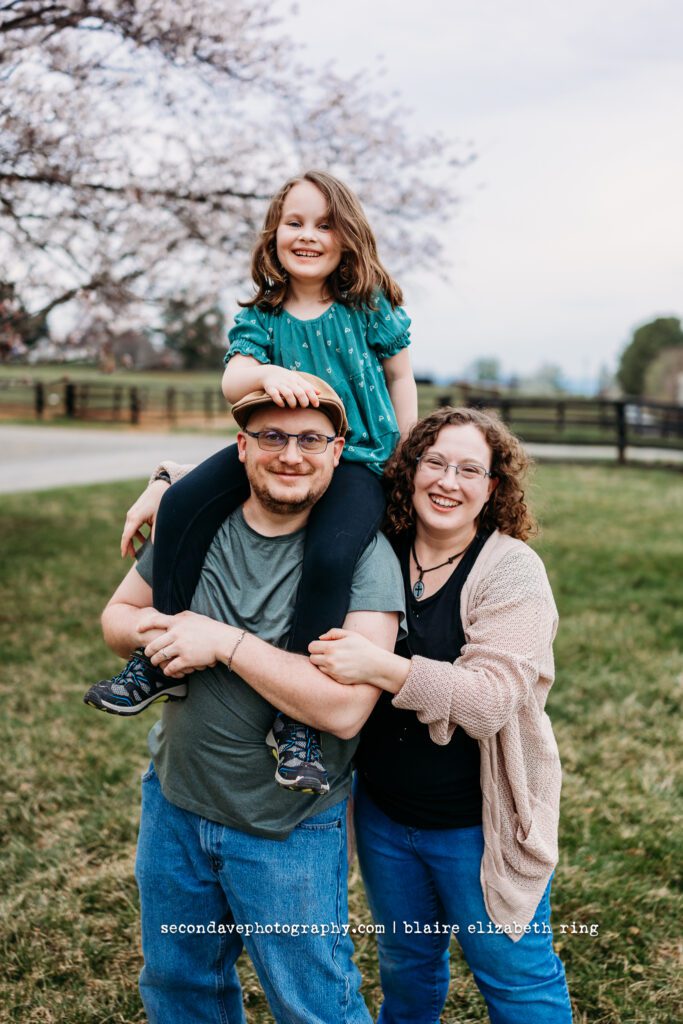 Family of 3 in front of blooming cherry blossoms in Northern Virginia.