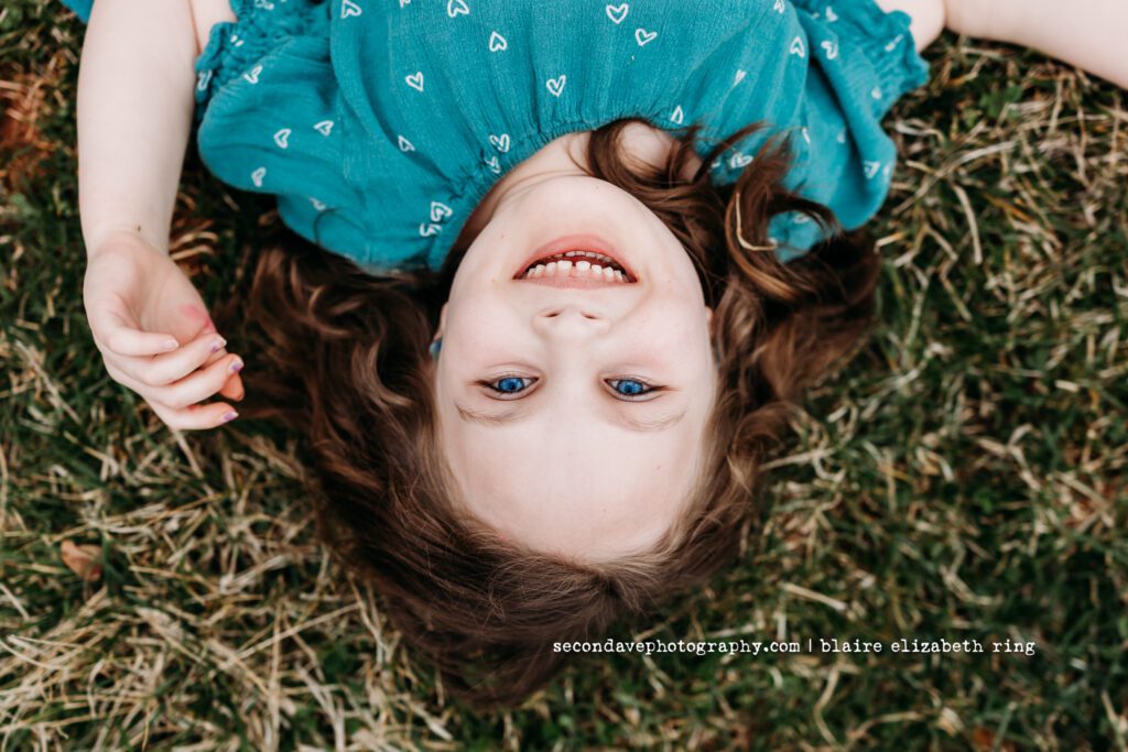 Smiling girl with extraordinarily bright blue eyes laying in the grass.