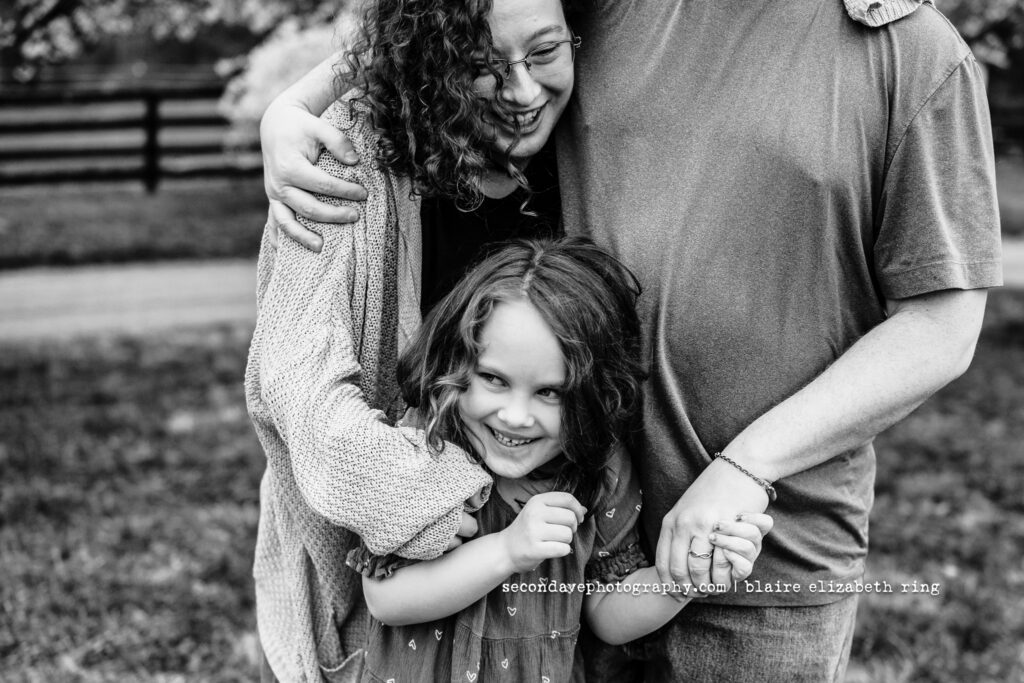 Black and white photo of family of 3 in front of blooming cherry blossoms in Northern Virginia.