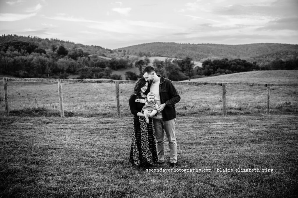 Black and white family photo in front of mountains with parents and baby at Sky Meadows State Park in Virginia.