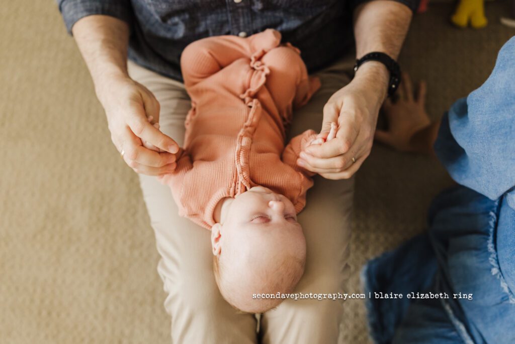 Lifestyle newborn photo of dad holding new baby's hands.